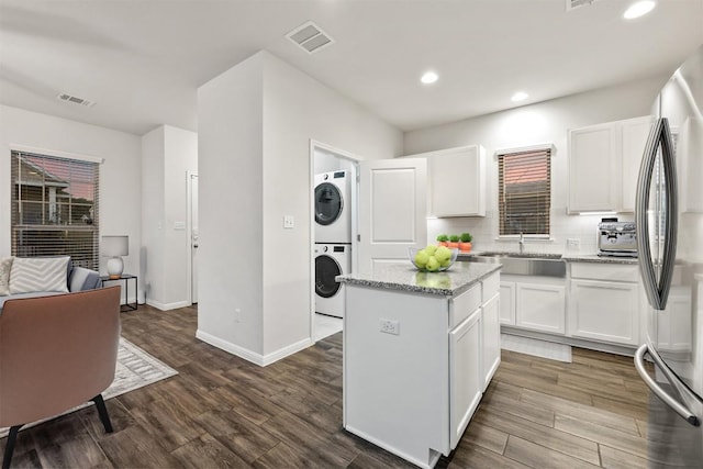 kitchen with dark wood-style flooring, decorative backsplash, white cabinets, stacked washer and clothes dryer, and a center island