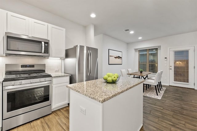 kitchen with tasteful backsplash, light stone counters, stainless steel appliances, wood finished floors, and white cabinetry