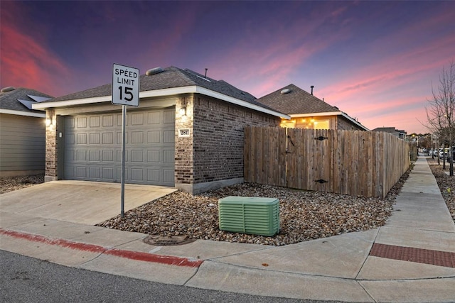 property exterior at dusk featuring fence, concrete driveway, a garage, central air condition unit, and brick siding