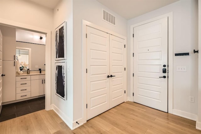 foyer entrance with light wood-type flooring, baseboards, and visible vents