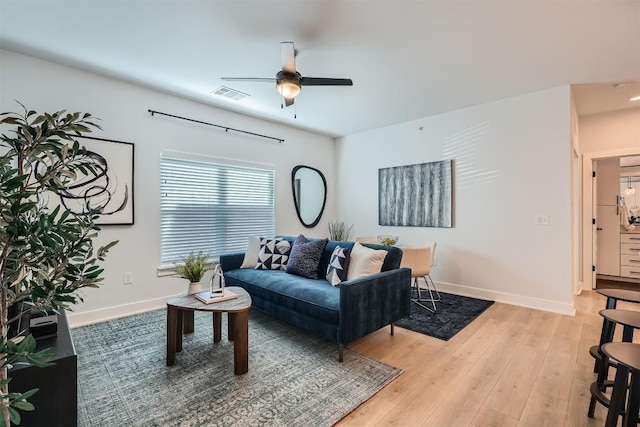 living room featuring light wood finished floors, baseboards, visible vents, and ceiling fan