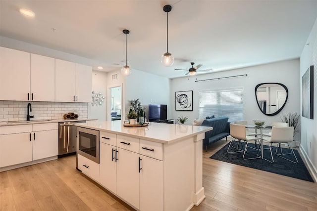 kitchen with a sink, light countertops, stainless steel dishwasher, built in microwave, and light wood finished floors