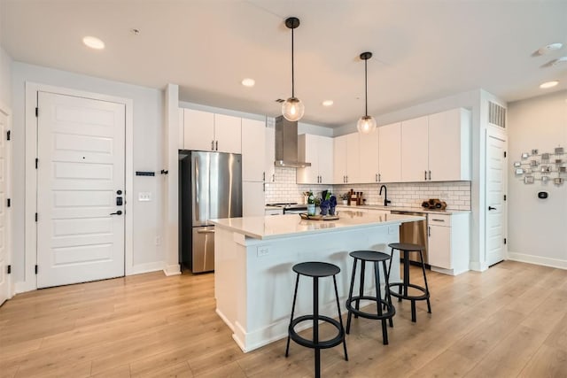 kitchen featuring a sink, visible vents, a kitchen breakfast bar, appliances with stainless steel finishes, and wall chimney exhaust hood