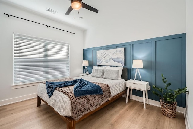 bedroom with light wood-style floors, ceiling fan, visible vents, and a decorative wall