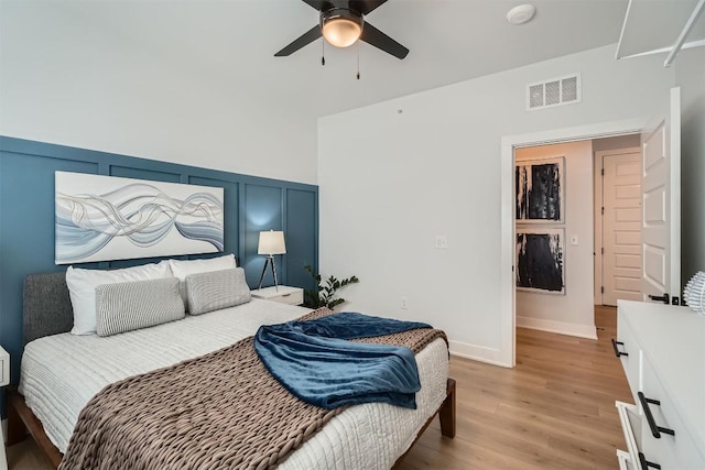 bedroom featuring light wood finished floors, visible vents, wainscoting, ceiling fan, and a decorative wall