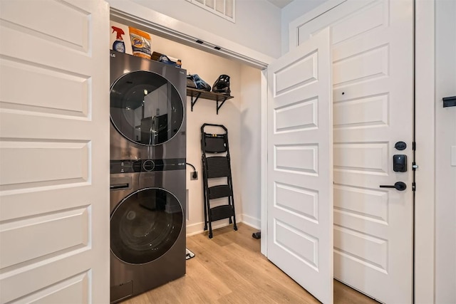 washroom featuring laundry area, baseboards, visible vents, stacked washer / drying machine, and light wood-style floors