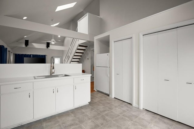 kitchen with lofted ceiling with skylight, ceiling fan, freestanding refrigerator, light countertops, and a sink