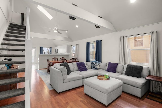 living room featuring stairway, lofted ceiling with skylight, wood finished floors, and a ceiling fan