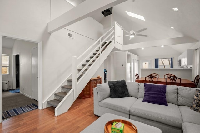 living room featuring high vaulted ceiling, a skylight, stairway, and wood finished floors