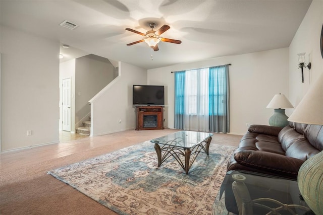 living area featuring light carpet, stairway, a glass covered fireplace, and visible vents