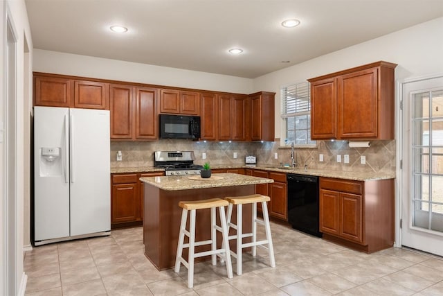 kitchen with light stone counters, backsplash, a sink, a kitchen island, and black appliances