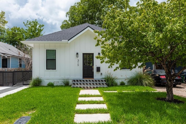 view of front of home featuring roof with shingles, board and batten siding, a front yard, crawl space, and fence