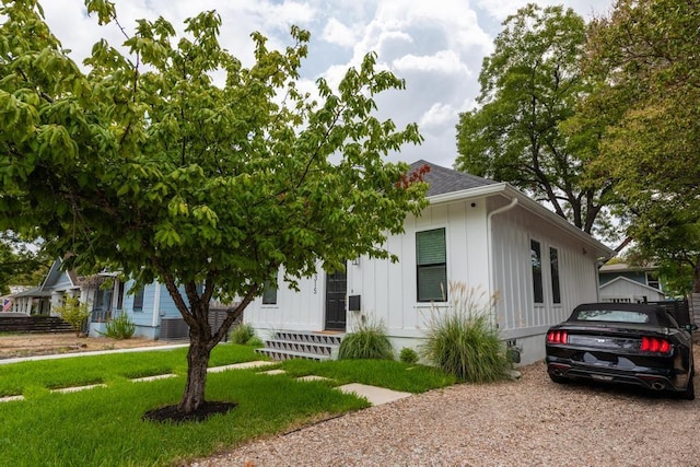 view of front of property with board and batten siding, a front yard, central AC, and a shingled roof