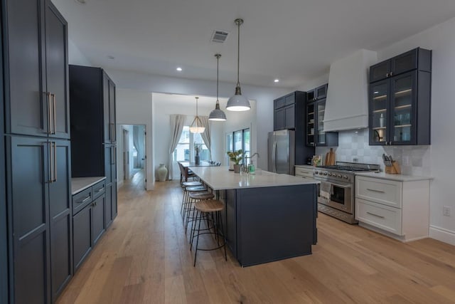 kitchen with visible vents, appliances with stainless steel finishes, a breakfast bar, glass insert cabinets, and custom exhaust hood