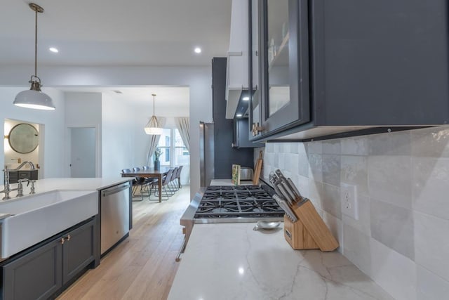 kitchen with dishwasher, light wood-style flooring, hanging light fixtures, light stone countertops, and backsplash