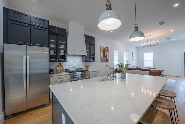 kitchen featuring decorative backsplash, a breakfast bar, light stone countertops, stainless steel appliances, and premium range hood