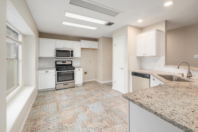 kitchen with visible vents, white cabinets, appliances with stainless steel finishes, light stone counters, and a sink