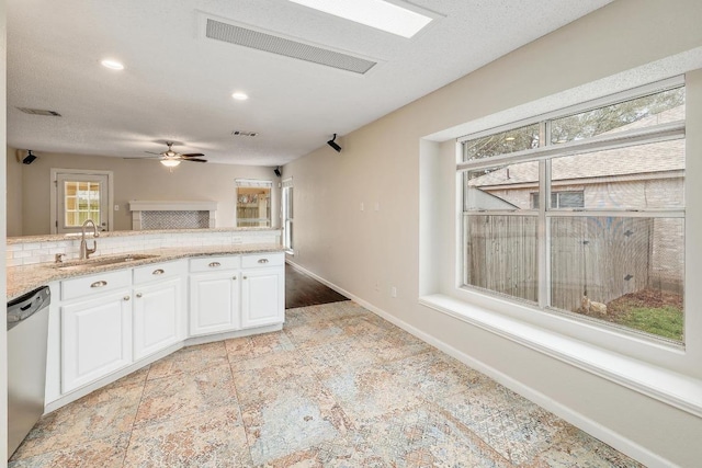 kitchen with light stone countertops, a sink, white cabinets, stainless steel dishwasher, and decorative backsplash