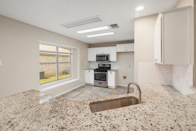 kitchen with stainless steel appliances, a sink, visible vents, white cabinets, and light stone countertops