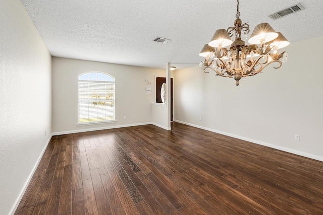 empty room featuring visible vents, dark wood-type flooring, a textured ceiling, a chandelier, and baseboards