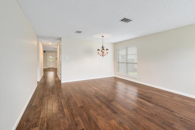 unfurnished room with visible vents, dark wood finished floors, baseboards, and an inviting chandelier