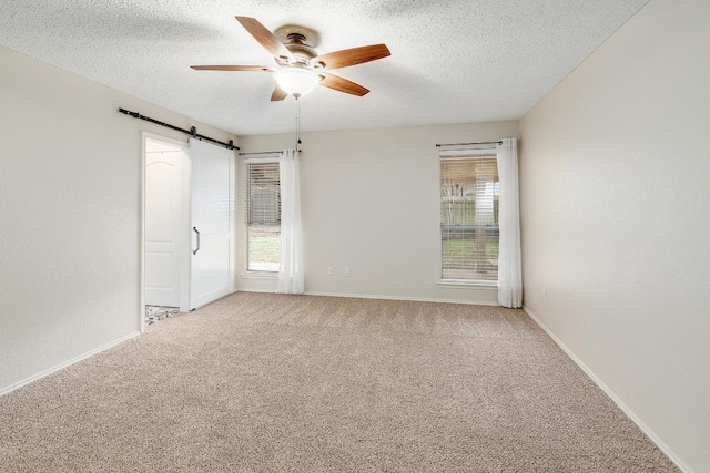 unfurnished room with ceiling fan, carpet floors, a barn door, and a textured ceiling