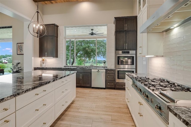 kitchen with dark brown cabinetry, dark stone counters, stainless steel appliances, under cabinet range hood, and backsplash