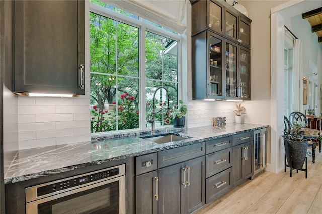 kitchen featuring stone countertops, decorative backsplash, wine cooler, light wood-type flooring, and a sink