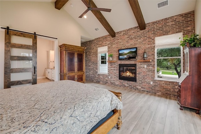 bedroom with high vaulted ceiling, a barn door, visible vents, light wood-type flooring, and a brick fireplace