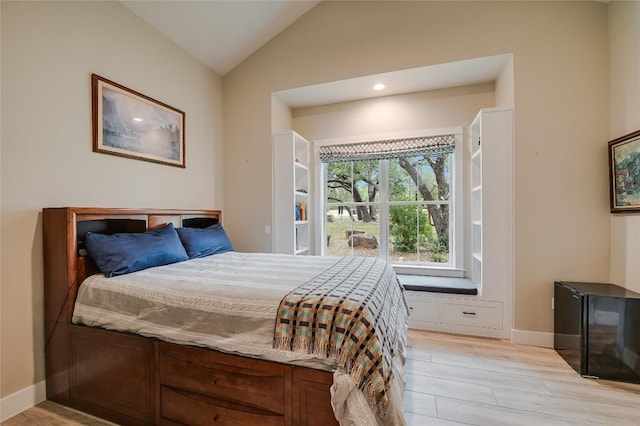 bedroom with light wood-type flooring, baseboards, and vaulted ceiling