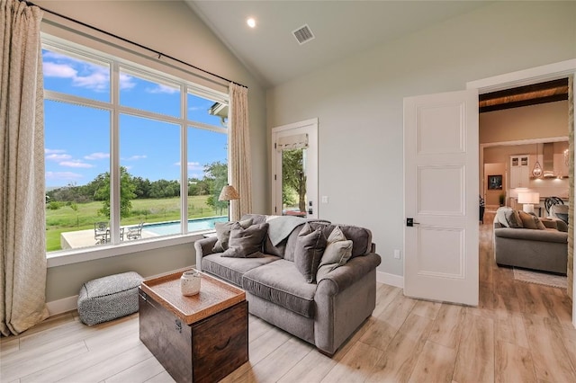 living room featuring high vaulted ceiling, light wood-type flooring, visible vents, and baseboards