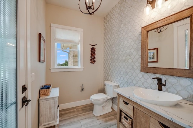 bathroom with toilet, wood finished floors, vanity, baseboards, and an inviting chandelier