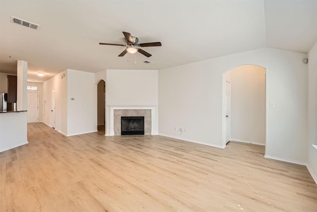 unfurnished living room featuring arched walkways, a tile fireplace, visible vents, and light wood-style floors