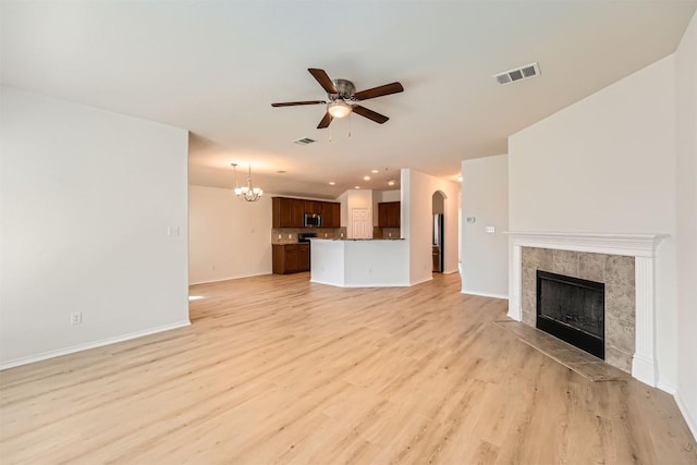 unfurnished living room with visible vents, arched walkways, light wood-type flooring, a fireplace, and ceiling fan with notable chandelier