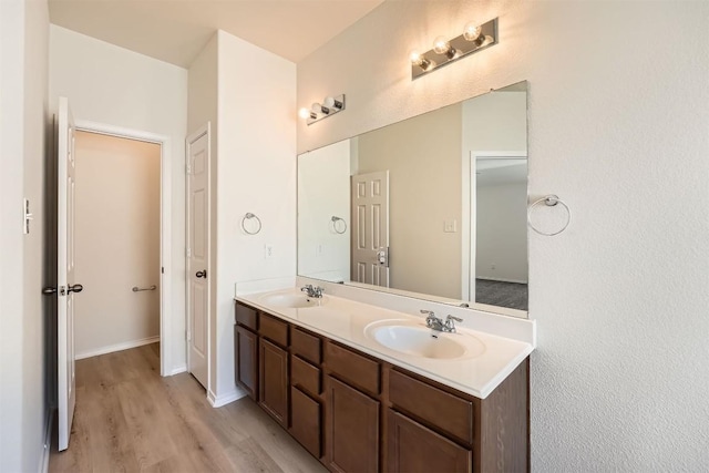 bathroom featuring double vanity, wood finished floors, a sink, and baseboards