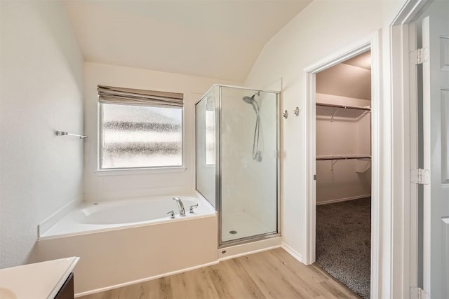 full bath with a walk in closet, a stall shower, vanity, wood finished floors, and a bath