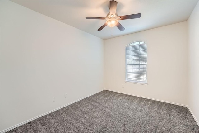 spare room featuring ceiling fan, dark carpet, and baseboards