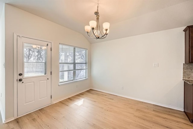 unfurnished dining area featuring baseboards, lofted ceiling, a chandelier, and light wood-type flooring
