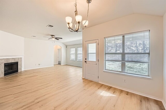 unfurnished living room featuring vaulted ceiling, arched walkways, a tile fireplace, and light wood-style floors