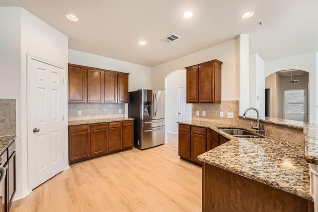 kitchen featuring light stone counters, arched walkways, visible vents, a sink, and stainless steel fridge