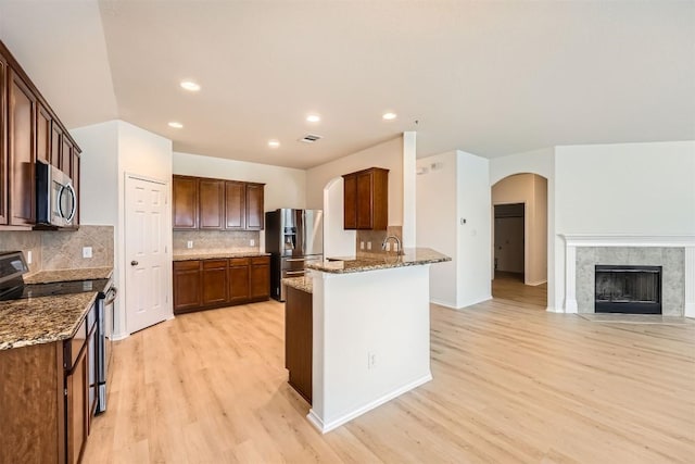 kitchen featuring open floor plan, appliances with stainless steel finishes, stone counters, and arched walkways