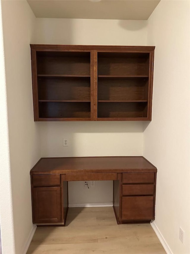 unfurnished office featuring light wood-type flooring, built in study area, and baseboards