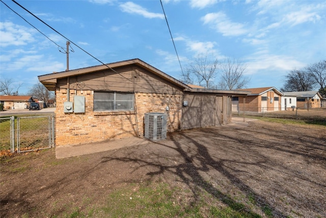 back of property with brick siding, a gate, fence, cooling unit, and driveway