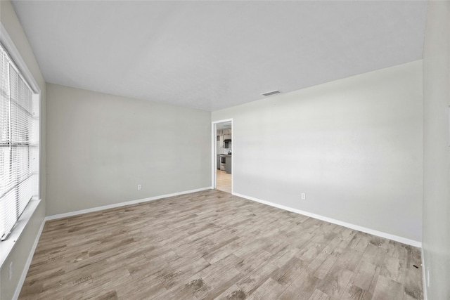 empty room with wood finished floors, visible vents, and baseboards