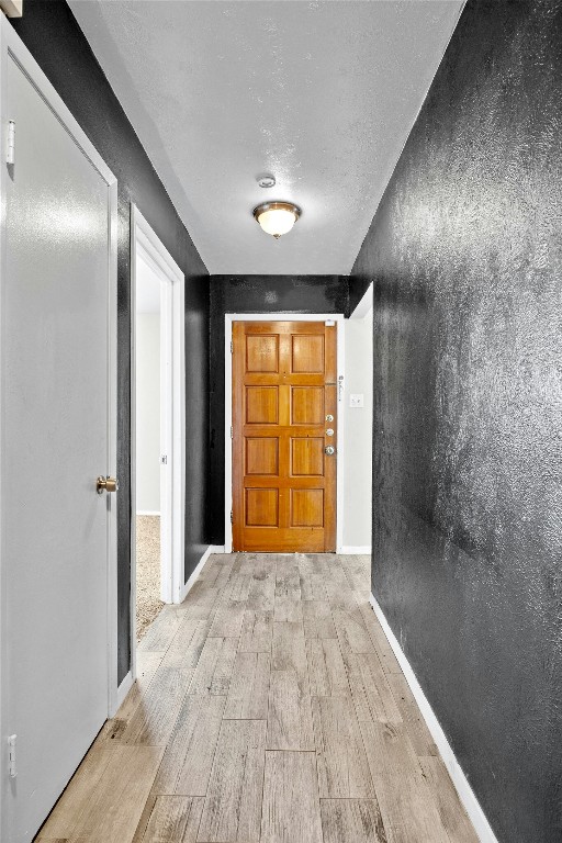 hall featuring a textured ceiling, baseboards, and wood finished floors