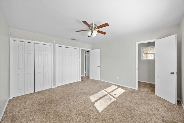 unfurnished bedroom with ceiling fan, visible vents, baseboards, multiple closets, and carpet