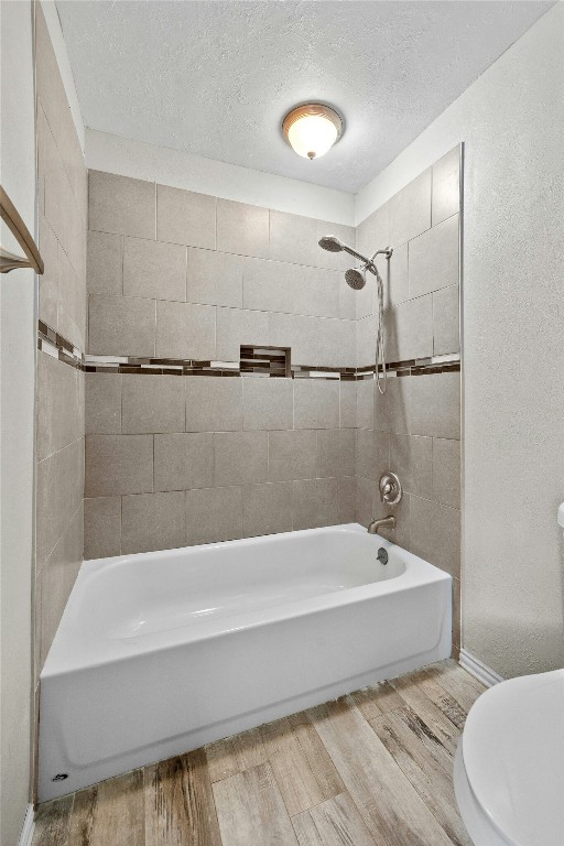 full bathroom with a textured ceiling, tub / shower combination, wood finished floors, and toilet