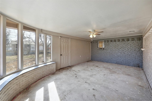 empty room featuring concrete flooring, brick wall, and ceiling fan