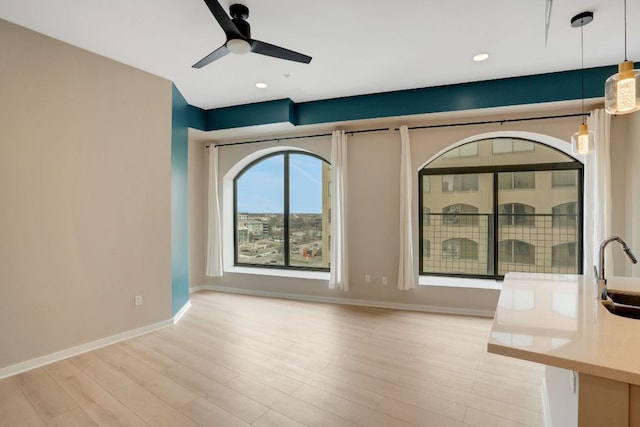 interior space featuring baseboards, a ceiling fan, light wood-type flooring, a sink, and recessed lighting