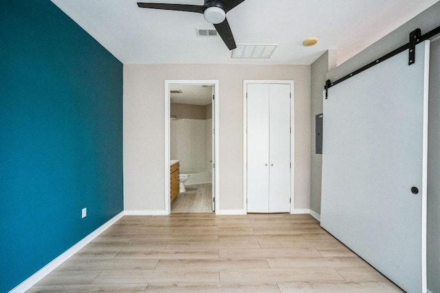 unfurnished bedroom featuring ensuite bathroom, a barn door, visible vents, baseboards, and light wood-style floors